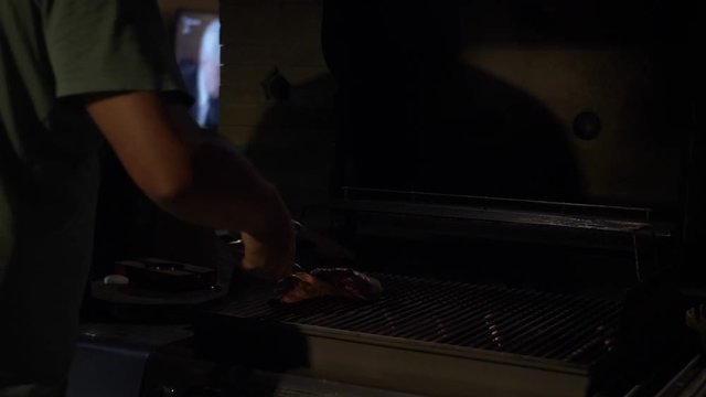 SLOW MOTION: Man holding tongs preparing fresh Flank Steak from USA on barbecue grill and turns meat with dripping into fire.