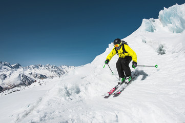 Professional skier at the speed before jumping from the glacier in winter against the blue sky and mountains