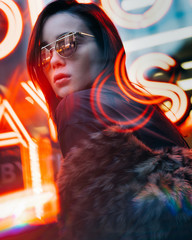 Fashionable girl in trendy fur coat and modern glasses with neon lights