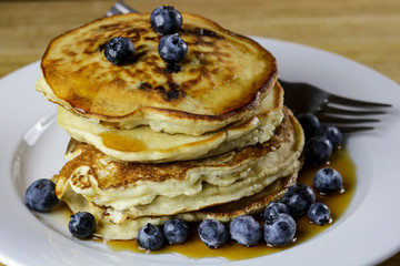 A stack of freshly prepared blueberry pancakes topped with maple syrup and fresh blueberries