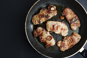 Pork steaks on a frying pan, black background, top view.
