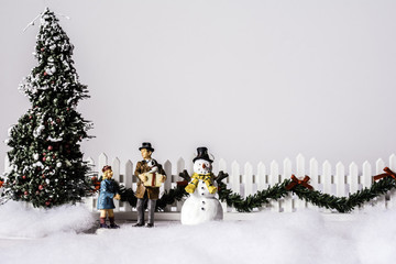 a snow covered Christmas scene with father and daughter between decorated tree and snowman picket fence with garland on white background with room for copy