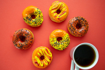 Halloween and Autumn colored tasty colorful donuts served for breakfast on a kitchen table with piping hot coffee.