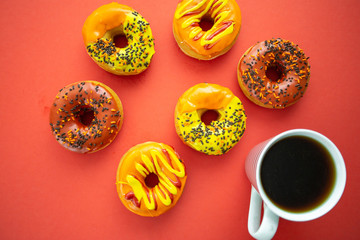Halloween and Autumn colored tasty colorful donuts served for breakfast on a kitchen table with piping hot coffee.