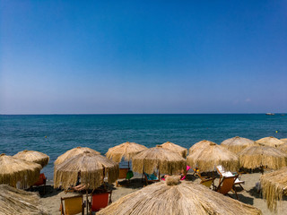 Viele Sonnenschirme aus Stroh am Strand mit Meer und blauen Himmel