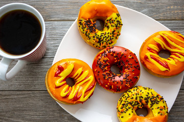 Halloween and Autumn colored tasty colorful donuts served for breakfast on a kitchen table with piping hot coffee.