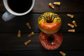 Halloween and Autumn colored tasty colorful donuts served for breakfast on a kitchen table with piping hot coffee.