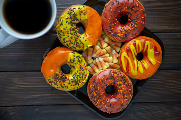 Halloween and Autumn colored tasty colorful donuts served for breakfast on a kitchen table with piping hot coffee.