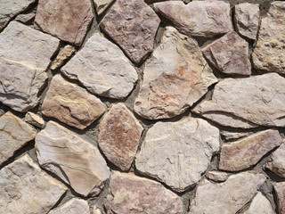 A wall of coarse stone and cement of pink and grey shades.