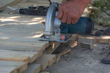 Electric circular saw is being cut a piece of wood by carpenter. Construction details of male worker. Formwork for the fence.