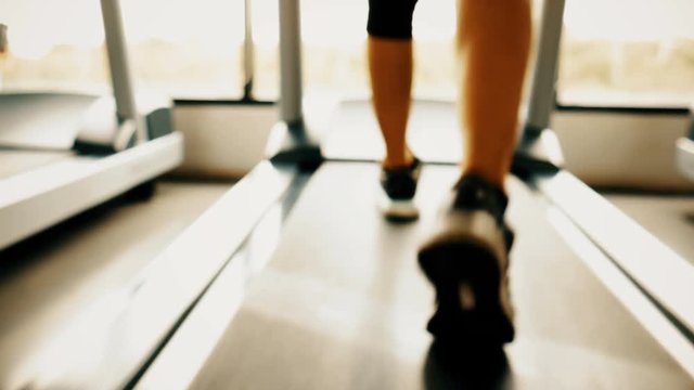 Close up blurry of sport woman legs running on treadmill in fitness gym sport center with window and sun light background. Exercise workout of diet and fat burning for healthy and wellness lifestyle.