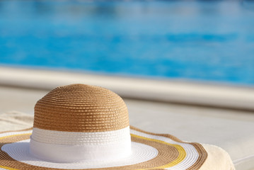 Fototapeta na wymiar Bonnet hat on sunbed against swimming pool.