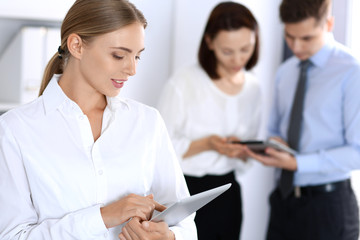 Beautiful blonde business woman using tablet or touch-pad on background of colleagues in office