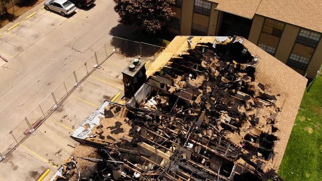 Footage of a burned down building, which is getting demolished with an excavator. The drone slowly flies over the scene and captures it in an aerial manner.