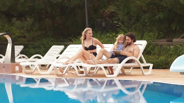 Relaxed young family sitting on sun loungers together near swimming pool