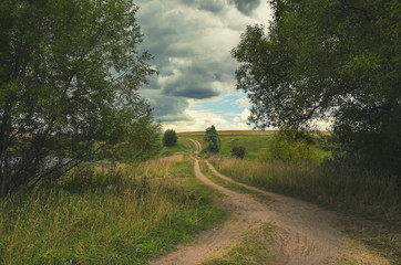 Cloudy summer landscape with ground country road.Dark stormy clouds in dramatic overcast sky.Fields,green meadows and woods.Tula region,Russia
