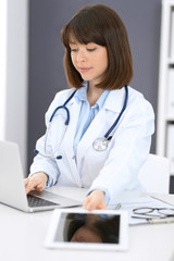 Doctor typing on laptop computer while sitting at the white table in hospital office. Physician at work. Medicine and healthcare concept