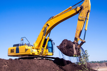 A large iron excavator bucket collects and pours sand rubble and stones in a quarry at the construction site of road facilities