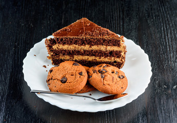 a piece of chocolate cake and cookies with chocolate on a red plate on a dark wooden background. Homemade baking.Close-up view.