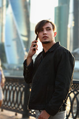 Fototapeta premium Young thinking casual man walking on the street and talking on mobile phone on city center background