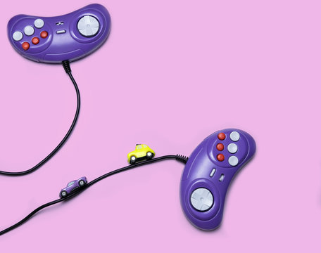 Two Retro Computer Gaming Controllers And Small Race Cars On The Pastel Pink Background Top View Space For Text Minimal Style