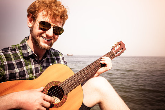 Young man hipster playing guitar by sea ocean.