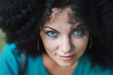 Sensual close-up portrait of young pretty woman with african curly hairstyle and nose piercing. Beautiful girl with green eyes smiling to camera at summer outdoors. Funny lady.