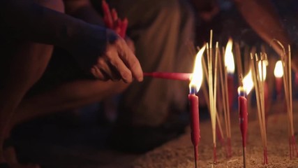 Close Up Of Worshiper Hand Light Up The Red Candle And Stick On The Sand