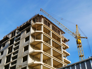Construction crane and concrete building under construction against blue sky. Construction site.