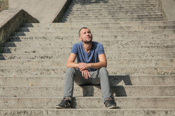 Fototapeta premium the man is sitting on the steps of the staircase in a relaxed pose on a sunny afternoon