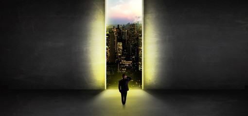Businessman standing in a dark room and looking outside to a cityscape view
