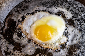 An egg frying in butter and oil in a carbon steel skillet