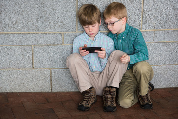 Two Young Boys Sitting on the Floor and Looking at a Mobile Phone Screen Together
