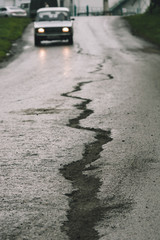 Long crack on asphalt and traveling car in front. Conceptual image in faded green tones.