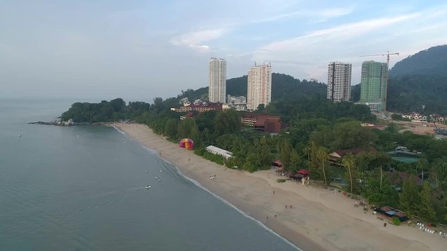 A drone shot of a parasailer behind the boat landing on the beach Batu Feringghi in  Penang, Malaysia.
