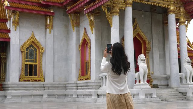 A woman walking in a temple in bangkok and stops to take a photo.
