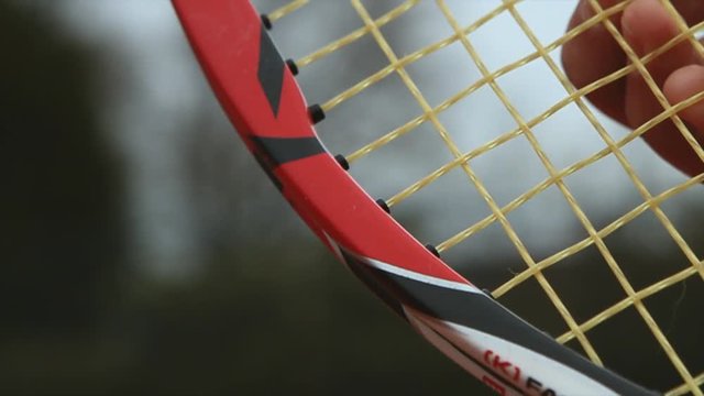 Tennisplayer plucking strings of a tennis racquet.