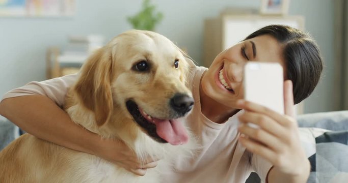 Close up of the cheerfulprety young woman taking selphie photos on the camera of her telephone and hugging a dog. Portrait.
