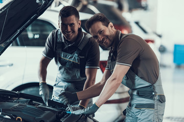 Two Mecanics Looking at Camera while Fixing Car