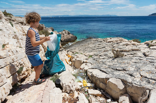 Little Boy Cleaning Up Beach Full Of Rigid Plastic Bottles And Other Garbage Washed Out On Coast.