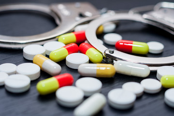 Handcuffs and pills and drugs on wooden table