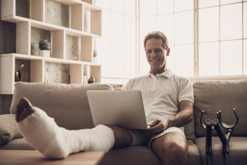 Man With Fractured Leg Sit On Sofa and Use Laptop