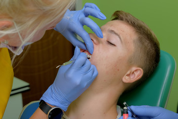 The doctor's hands attaching and holding brackets on the teenager's teeth with a special tool.