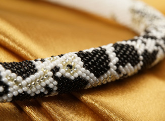 Bead rope, seed beads, bead necklace. Close up of white and black bead necklace on a gold satin