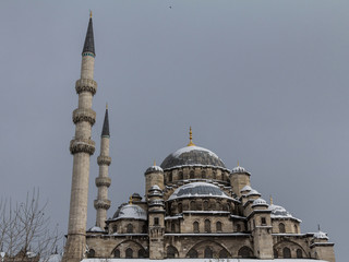 Fototapeta na wymiar Eminonu Mosque, also known as New Mosque, or Yeni Cami, in Istanbul, Turkey, covered in snow during a winter afternoon. It is one of the main ottoman landmarks and touristic attractions in the city