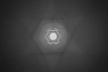 Black and white image of a lamp casting a star of David shadow on the ceiling