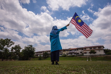 Girl waving the Malaysia Flag. Independence Day & Merdeka Concept. Blue sky and copy space.