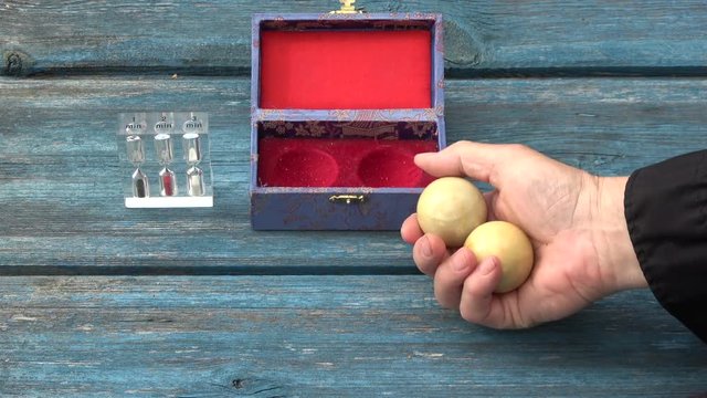 Chinese hand massage Baoding balls in hand and hourglass on old wooden garden table


