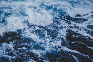 Dramatic foamy sea top view near the rocky shoreline, toned abstract image