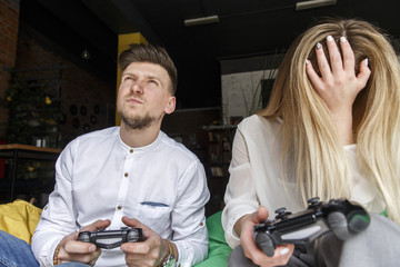 Fototapeta na wymiar Concentrated man is holding gamepad and looking up. He is nervous. Girl is holding gamepad as well and covering face with hand. She is ashamed.